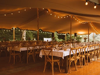 Banquet sous une tente stretch avec rangées de tables dressées et guirlandes lumineuses