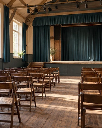 An empty theatre rehearsal space in warm late-afternoon light, rows of chairs facing a bare, quiet stage.