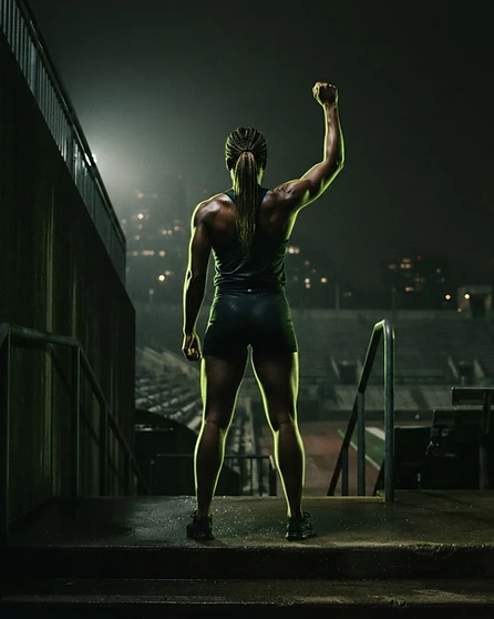Atleta de costas erguendo o punho em vitória no topo de escadas de estádio à noite