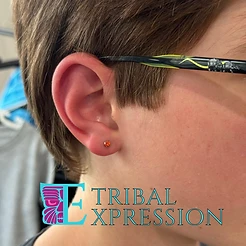 A close-up of a child’s earlobe with a small round orange stud earring.