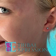 A smiling child in profile with a small light-blue dome stud earring in the earlobe.