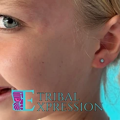 A smiling child in profile with a small light-blue dome stud earring in the earlobe.