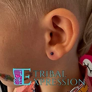 A close-up of a child’s earlobe with a polished metallic blue ball stud earring.