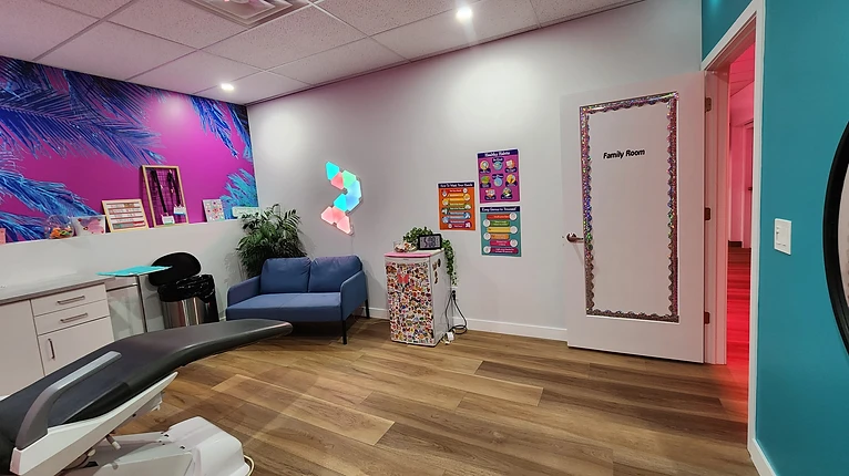 The kids piercing room with a bright mural, a comfy blue seat, and the Family Room door.