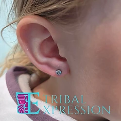 A close-up of a child’s earlobe with a small light-blue gemstone stud earring.