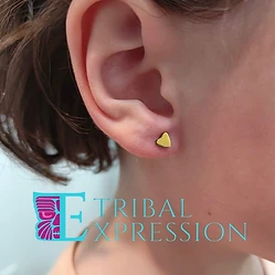 A close-up of a child’s earlobe with a small gold heart-shaped stud earring.