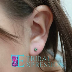 A close-up of a child’s earlobe with a small green gemstone stud earring.
