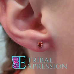 A close-up of a person’s earlobe with a round orange gemstone stud earring.