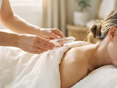 A therapist holding a Lemurian quartz crystal wand above a client draped in white linen