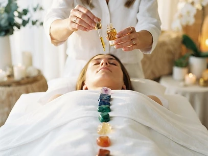 A practitioner anointing chakra gemstones placed along the body with golden essence