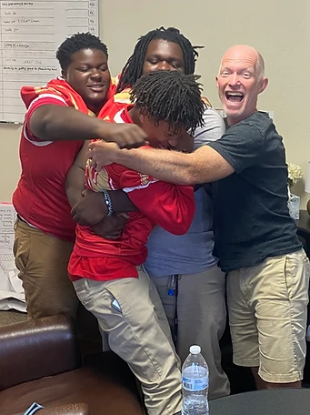 Four youth in a joyful group hug indoors