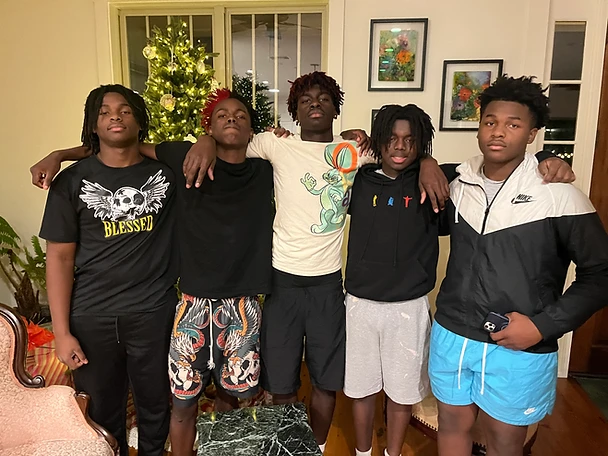 Five young men in a group portrait indoors beside a Christmas tree