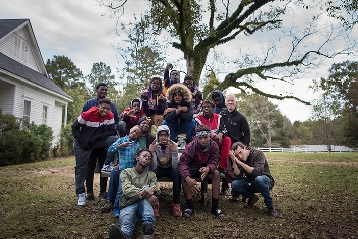 A group of young people posed together outdoors on a leafy lawn