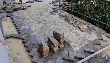 Clean pavers stacked beside the walkway with fresh bedding sand spread