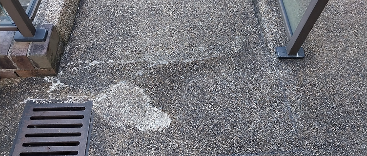 Close-up of worn pebblecrete with the damaged aggregate removed near a drain grate