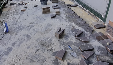 Pavers being re-laid in a herringbone pattern over fresh sand bedding