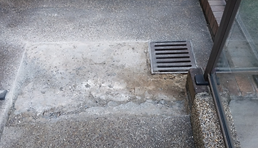 Bare concrete patch where damaged pebblecrete was removed next to a drain grate