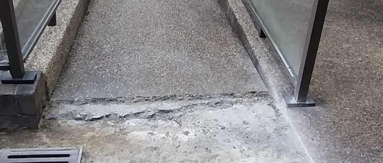Walkway with a recessed section of pebblecrete missing, exposing raw cracked concrete near the drain