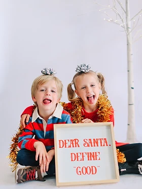 Brother and sister in gold tinsel holding a Dear Santa, define good sign