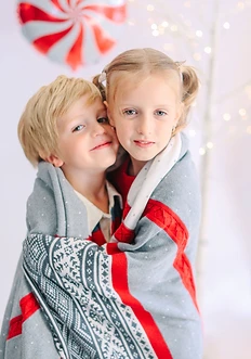 Brother and sister wrapped together in a red and grey knit blanket
