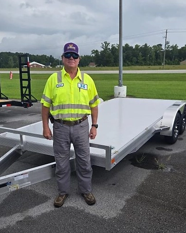 Kevin McCoy, Prime Trail Trailers sales and support agent in a high-visibility shirt on the dealership lot beside a flatbed trailer