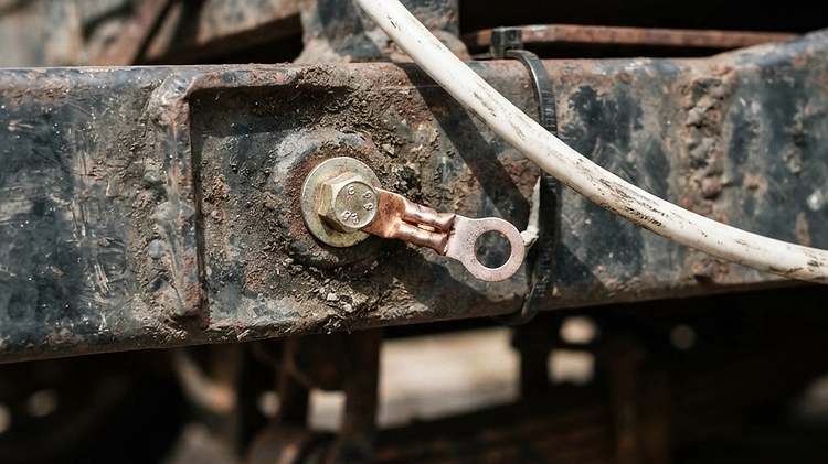 Corroded trailer ground wire bolted to a rusty steel frame