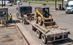 A heavy-duty flatbed trailer loaded with construction equipment parked on a scale