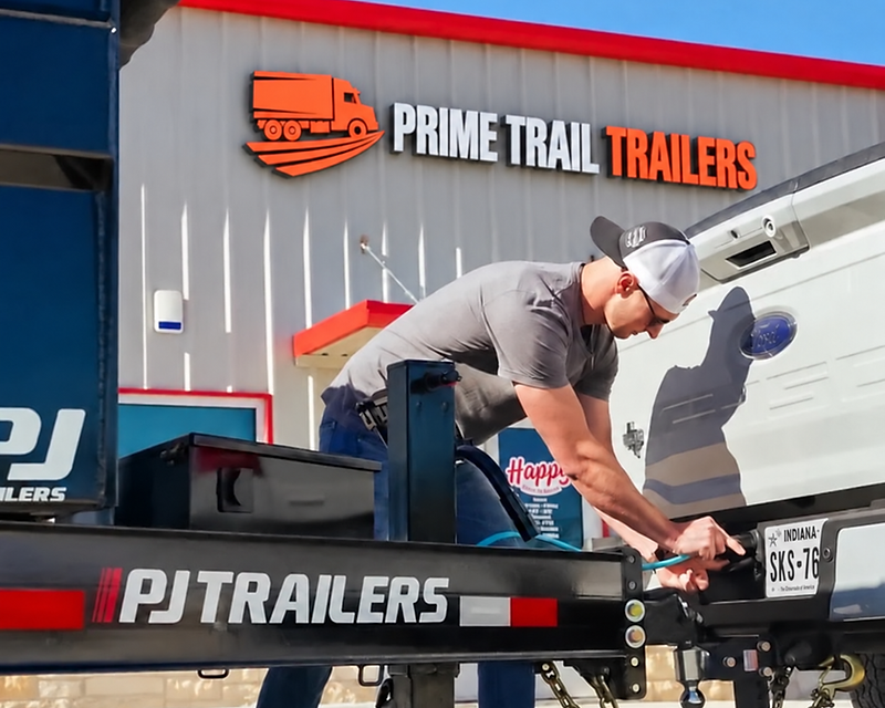 Prime Trail Trailers crew hitching a PJ flatbed trailer to a pickup truck at the dealership lot in Markle, Indiana