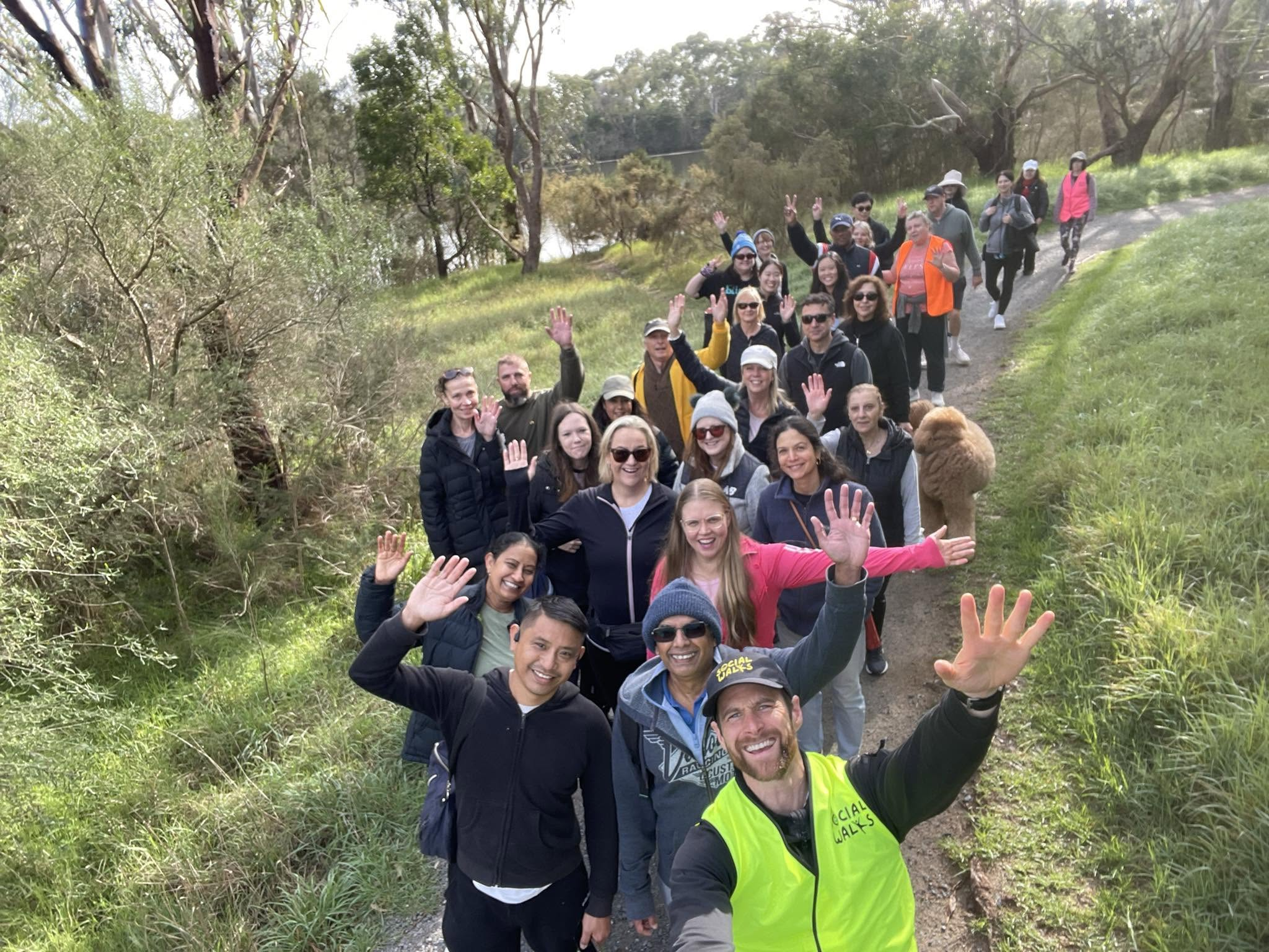 Large group walking a trail, volunteers waving at the camera