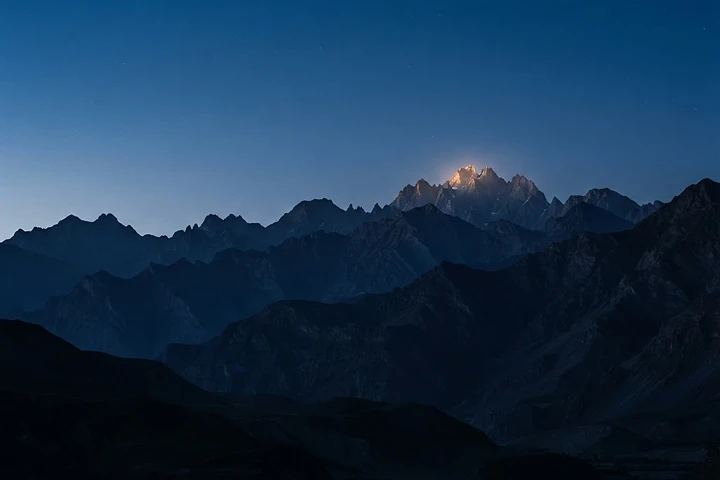 Mountain range silhouette at deep blue dusk with gold light on the peak