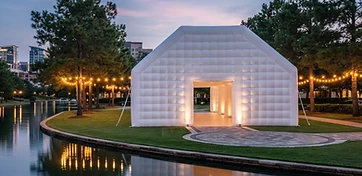 Grand white inflatable pavilion glowing at twilight beside a Houston waterway, compared to a traditional tent