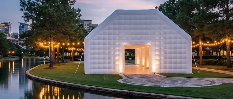 Grand white inflatable pavilion glowing at twilight beside a Houston waterway, compared to a traditional tent