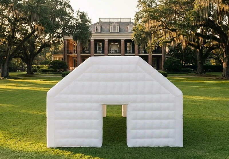 White inflatable wedding pavilion draped with floral garlands on a manicured estate lawn at golden hour