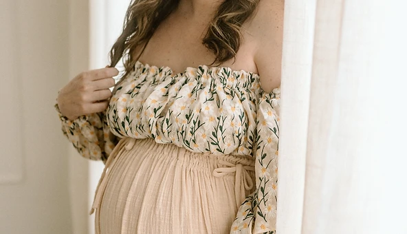 Expectant mother in profile beside a sheer curtain