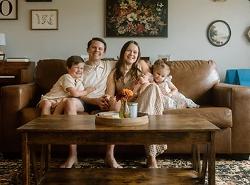 Family of five gathered on their living room couch with a newborn