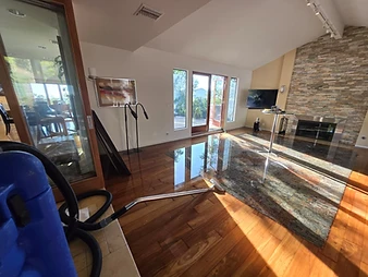 Blue water extraction vacuum and suction wand in a flooded living room with stone fireplace and vaulted ceiling