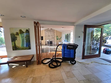 Blue KRAKEN water extraction vacuum on tiled floor with hose running into a flooded living room