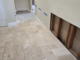 Hallway with stone tile floor and section of drywall cut out exposing wooden wall studs during restoration