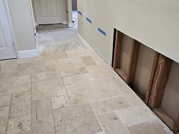 Hallway with stone tile floor and section of drywall cut out exposing wooden wall studs during restoration