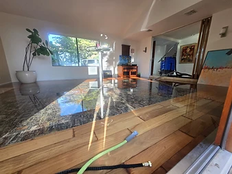 Flooded living room with green extraction hose across the floor, reflecting water on hardwood surfaces