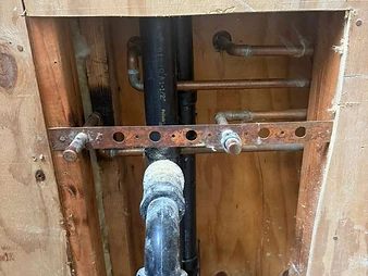 Open wall cavity between wooden studs showing black ABS pipe, P-trap, copper supply lines, and metal mounting strap