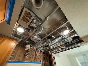 Ceiling cavity exposed during restoration showing metal grid tracks, foil-wrapped HVAC ducts, PEX pipe, and R-13 insulation