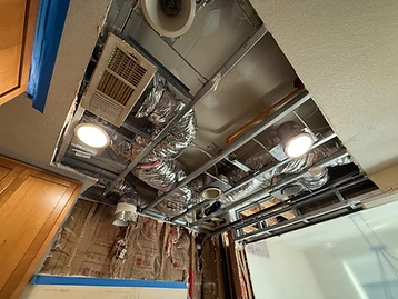 Ceiling cavity exposed during restoration showing metal grid tracks, foil-wrapped HVAC ducts, PEX pipe, and R-13 insulation