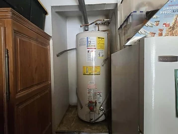 Residential water heater in a utility alcove with copper plumbing lines and metal exhaust vent