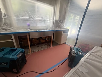 Kitchen containment zone with plastic sheeting, two XPOWER air movers, and opened under-sink area exposing wall studs