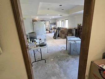 Room under renovation viewed through a wooden door frame, with drywall patches, bare concrete floor, and air scrubber equipment