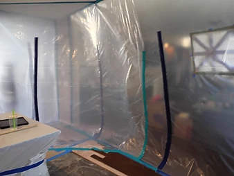 Temporary containment zone with plastic sheeting, mesh ventilation screen, and blue tape securing floor protection
