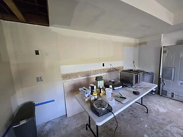 Room under repair with folding table holding supplies, exposed drywall patches, and open ceiling joists