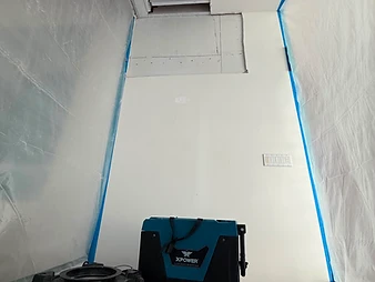 Two XPOWER LGR dehumidifiers on floor with drainage hose, open ceiling cavity, and containment plastic sheeting