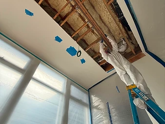 Worker in white Tyvek suit on a blue Werner stepladder reaching into an open ceiling section during restoration